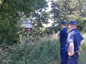 dwóch umundurowanych policjantów stojących przed tablicą