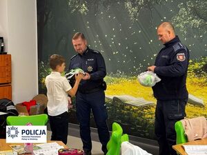 dwóch policjantów stoi i przekazuje chłopcu kask rowerowy