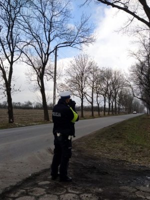 Na zdjęciu widać policjanta w mundurze trzymający ręczny miernik prędkości.